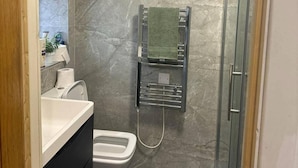 Egy fürdőszoba zuhanyzóval, WC-vel és mosdókagylóval.