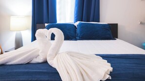 A hotel room with a bed, blue curtains, and two towels arranged in a swan shape. - Chris Home for 20 Guests - Private Pool & Jacuzzi (Ensenada)