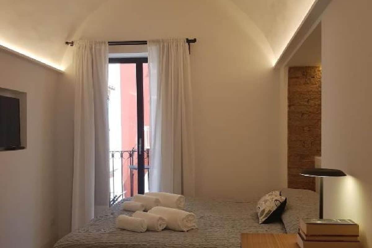 A bedroom with a bed, a bedside table with a lamp, a window with curtains, and a view of the outside.