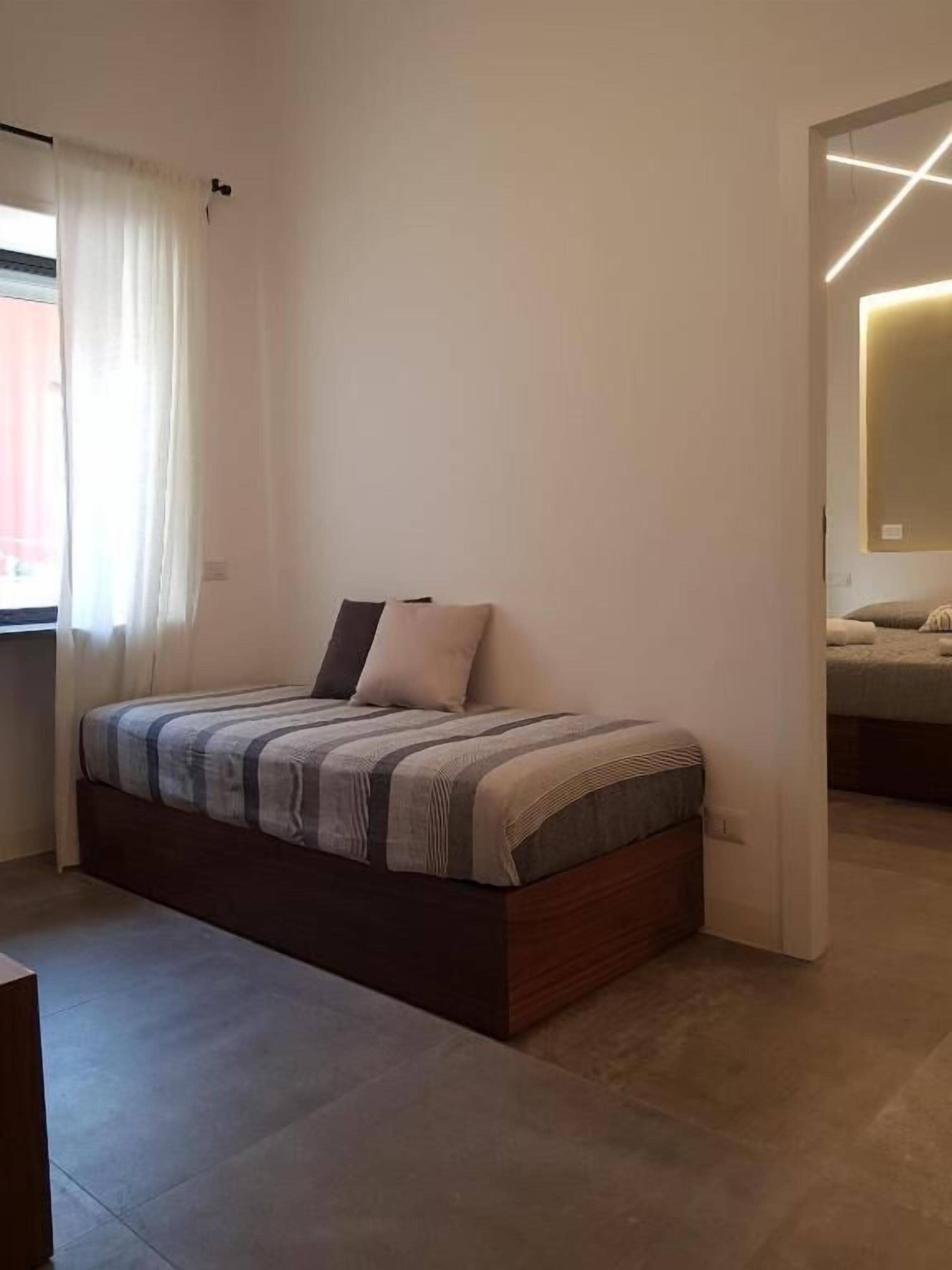 A modern bedroom with a bed, a window with curtains, and a visible bathroom.