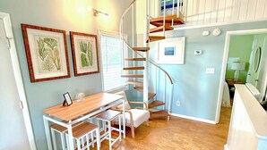 A modern kitchen with a wooden table, white chairs, a built-in stove, and a spiral staircase to an upper level. - Family Favorite Beach & Golf Condo with a View (Edisto Island)