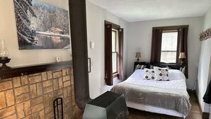 A cozy room with a fireplace, a bed with a large window, and a bookshelf. - The Pond Cottage at Rustic River (Austinburg)