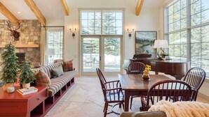 A spacious living area with a stone fireplace, a wooden ceiling, and large windows offering a view of the outdoors. - Luxury Mountain Estate w/ Indoor Pool, Gym & Hot Tub Near Keystone | Sleeps 19 (Keystone)