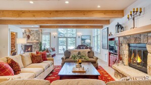 A spacious living room with a fireplace, a stone wall, and a large window. - Luxury Mountain Estate w/ Indoor Pool, Gym & Hot Tub Near Keystone | Sleeps 19 (Keystone)
