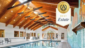 A spacious indoor swimming pool area with wooden beams on the ceiling, a view of the outdoors through large windows, and a sign indicating a 'Best Estate' award. - Luxury Mountain Estate w/ Indoor Pool, Gym & Hot Tub Near Keystone | Sleeps 19 (Keystone)