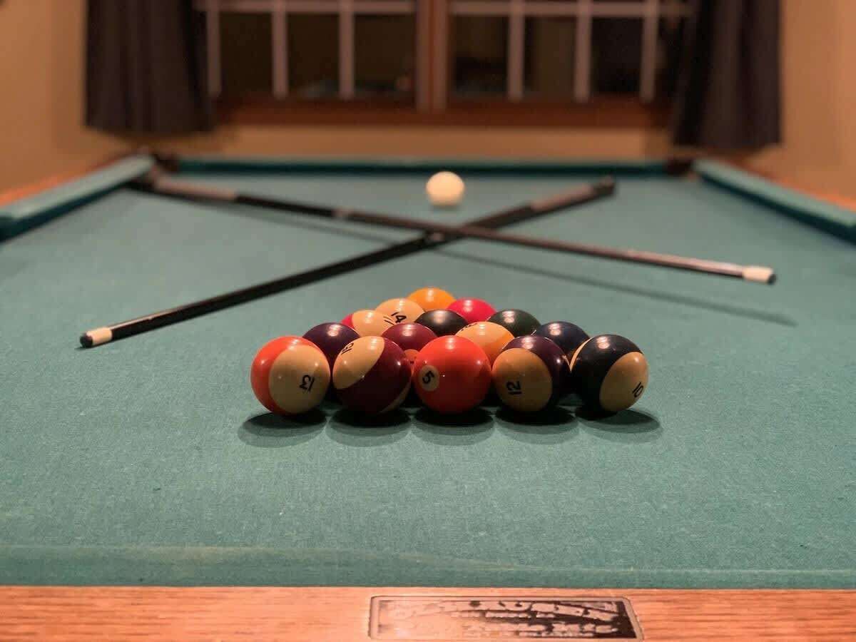 Une table de billard avec un jeu de billes et deux queues de billard.