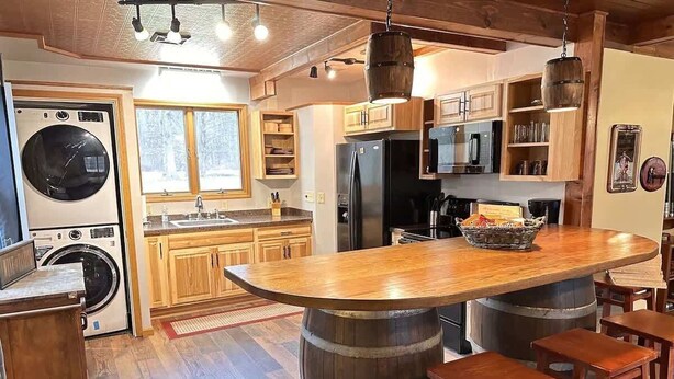 A kitchen with wooden cabinets, a large island with stools, a washing machine, and a refrigerator.