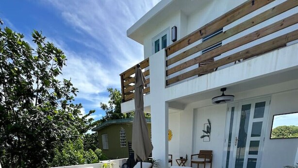 A modern outdoor lounge area with stone flooring, wooden furniture, and a view of a lush garden. - Casa Rosado @ Rincon Rayo Suite Mountain View Pool (Cruces)