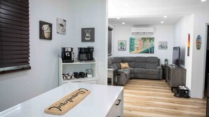 Una sala de estar moderna con un sofá gris, una cafetera y un televisor sobre un mueble de madera.