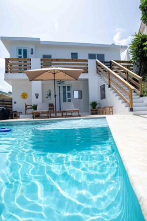 Ein modernes Haus mit Swimmingpool, Holzterrasse und Sitzbereich im Freien.