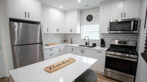 Una cocina moderna con armarios blancos, electrodomésticos de acero inoxidable, una isla central y un reloj en la pared.