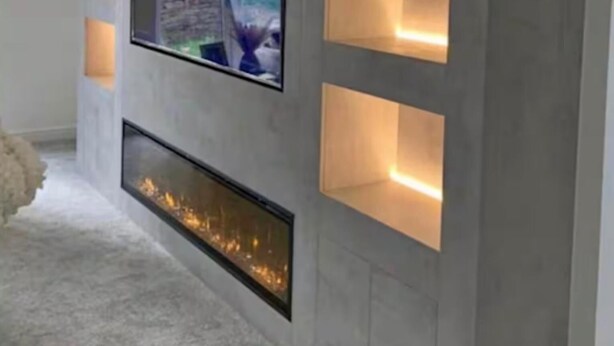 A modern living room with a flat-screen TV mounted on a gray wall, recessed shelves, and a built-in fireplace.
