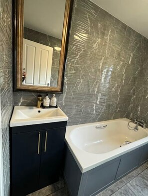 A bathroom with a white bathtub, a dark vanity with gold handles, and a large mirror above the sink.