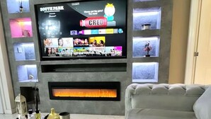 A modern living room with a large flat-screen TV mounted on a grey wall, a fireplace below, and a grey sofa.