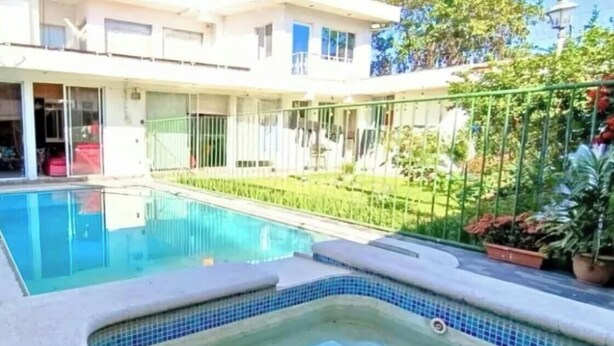 A swimming pool with a small hot tub area, surrounded by a green fence and potted plants. - Spacious 4 bedroom&Pool and 2 jacuzzis, WiFi, AC In Amazing area in San Salvador (San Salvador)