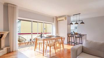 Una sala de estar moderna con sofá, mesa de comedor con sillas, chimenea y una zona de cocina con taburetes de bar.