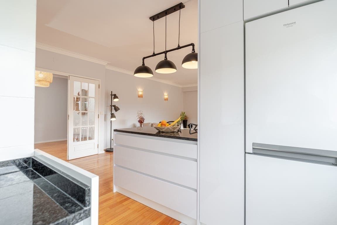 A modern kitchen with white cabinetry, a built-in refrigerator, a wooden countertop, and pendant lighting.