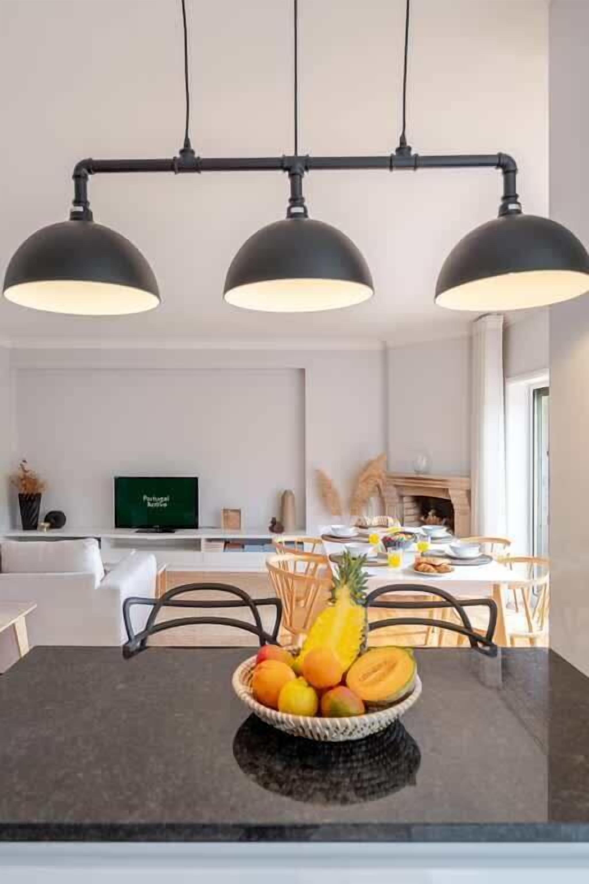 Ein moderner Essbereich mit einem schwarzen Tisch, einer Obstschale und einem Fernseher im Hintergrund.