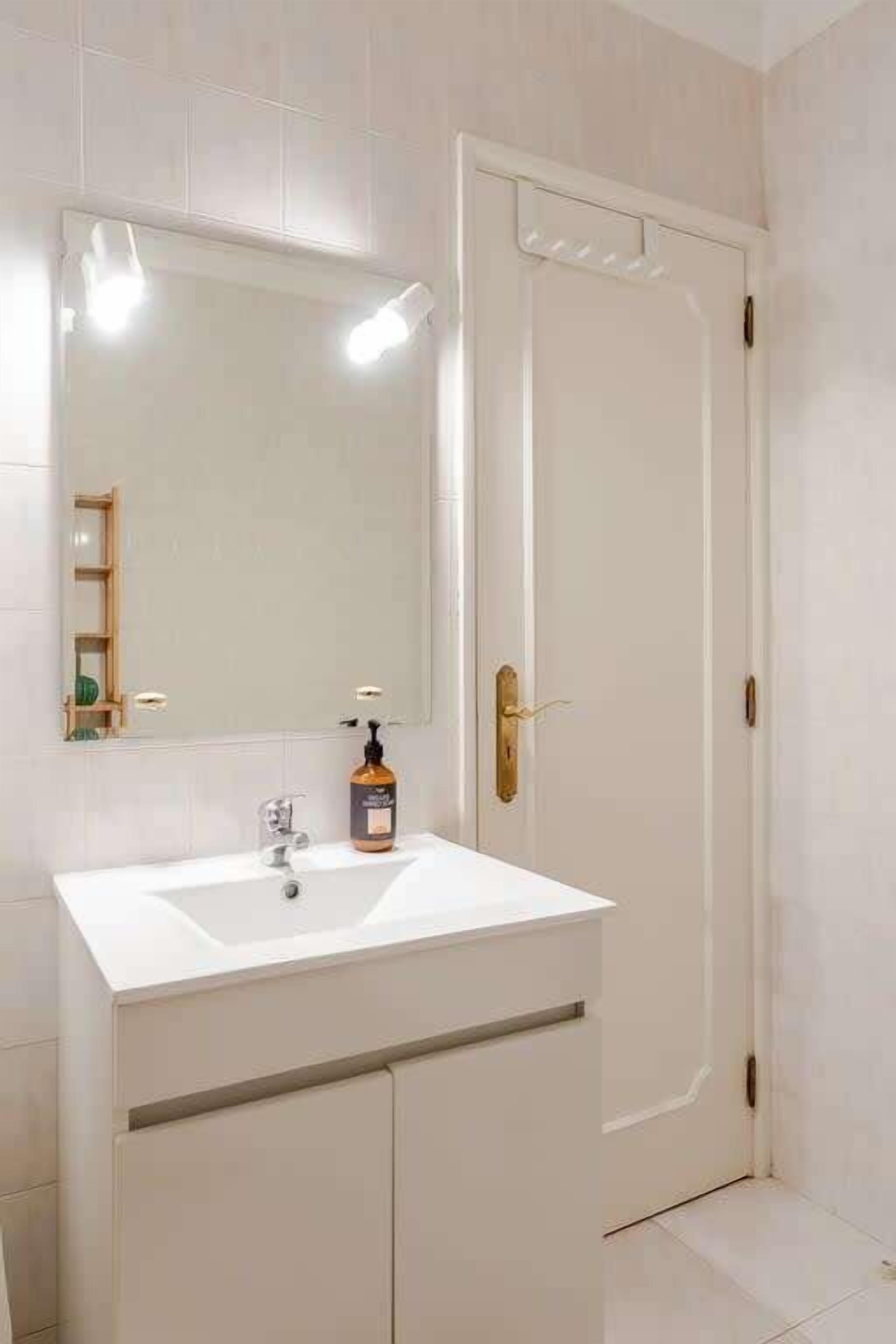 A bathroom with a white sink, a mirror, and a door with a gold handle.