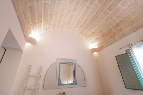 Une salle de bain avec un plafond blanc, un miroir doté d’un cadre décoratif, un porte-serviettes et une fenêtre avec un store vert.