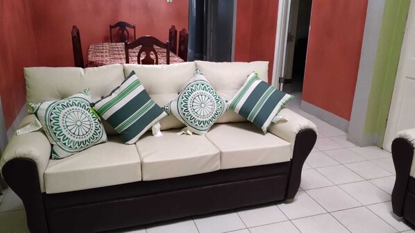 A beige sofa with dark cushions and patterned pillows in a room with red walls and a tiled floor. - Room-comfy Kingston Getaway - Private Ro (Kingston)