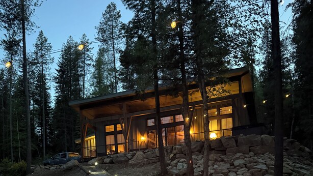 Ein modernes Haus mit steinernen Fundamenten und großen Fenstern, umgeben von einem Wald.