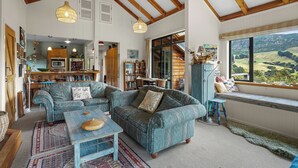 Un vaste espace de vie avec une grande fenêtre donnant sur la campagne, un coin salon confortable et une cuisine rustique en arrière-plan.