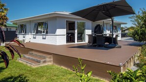 Ein modernes Haus mit überdachter Terrasse, Grillplatz und einer Glasschiebetür zum Außenbereich mit Sitzgelegenheit.