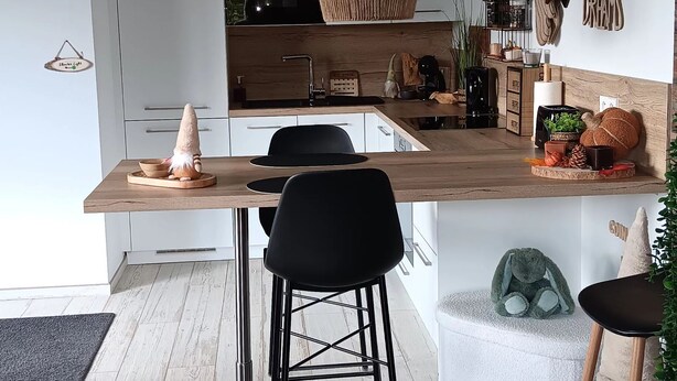 A modern kitchen with a central island, black bar stools, and a hanging light fixture.