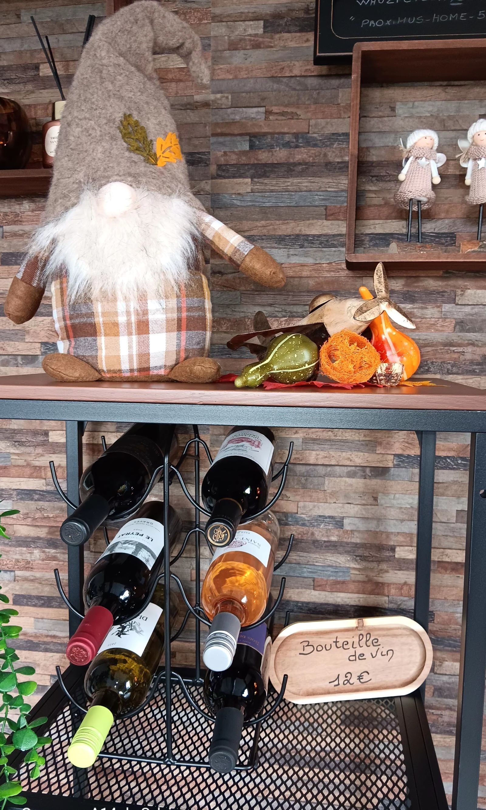 A rustic wooden table with a decorative gnome figure, a bottle of wine, and a sign indicating a price of 12€.