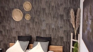 A bedroom with a wooden headboard, a bed with black and white patterned pillows, and a wall with a textured design.