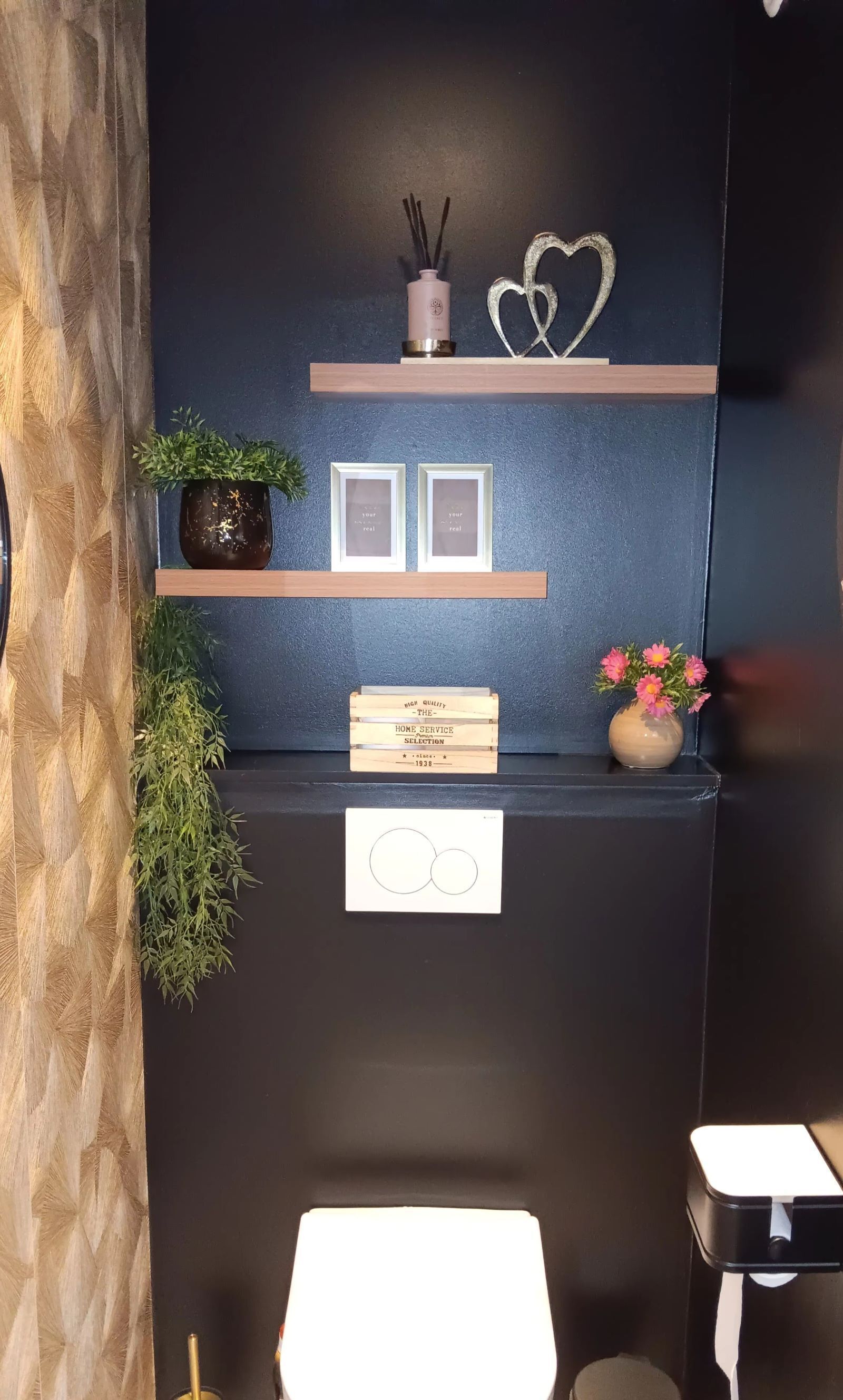 Una moderna recepción con una pared oscura, estantes de madera, una planta en maceta, cuadros enmarcados, una vela y un objeto decorativo con forma de corazón.