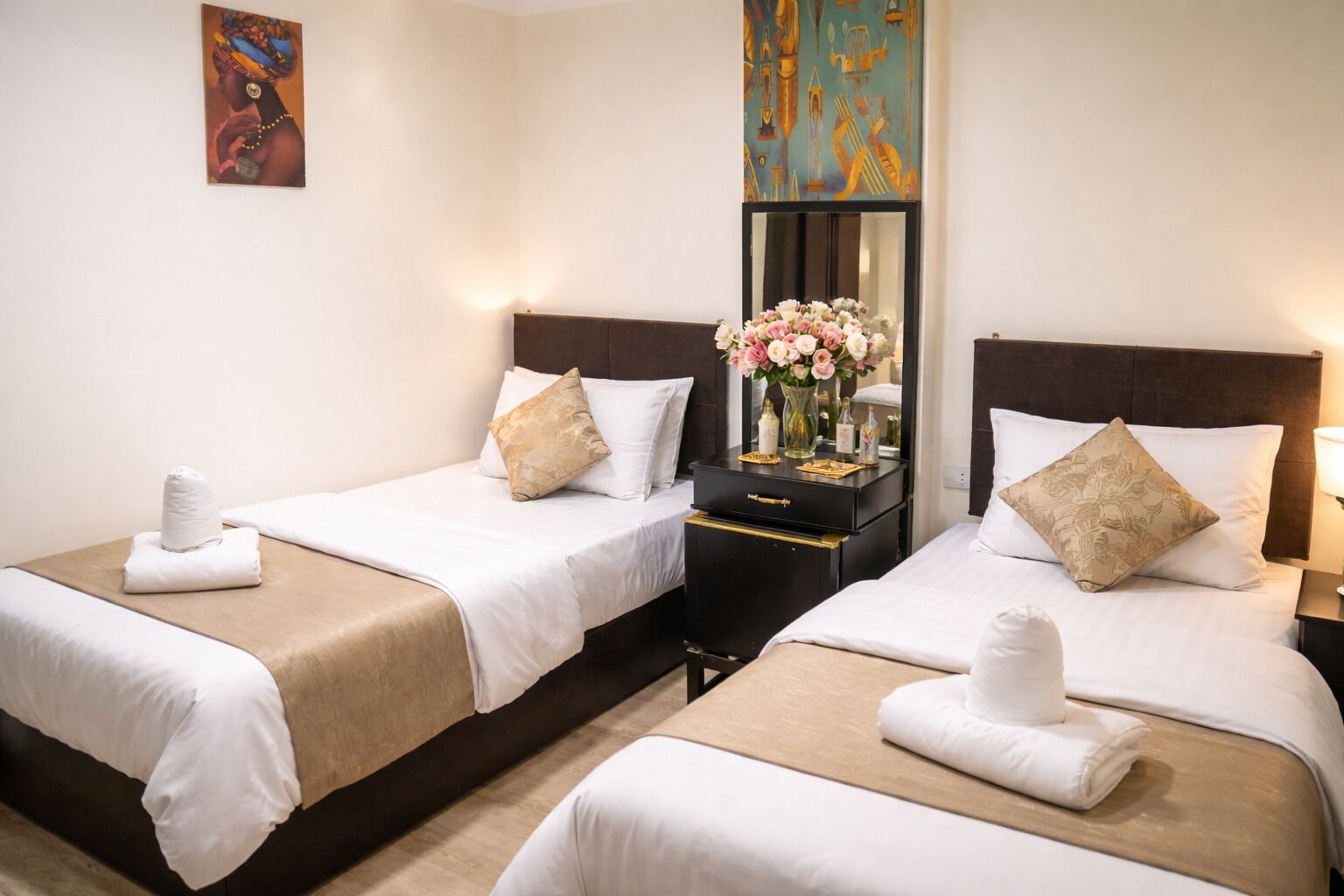 Habitación de hotel con dos camas, una mesita de noche, un espejo y un cuadro en la pared.
