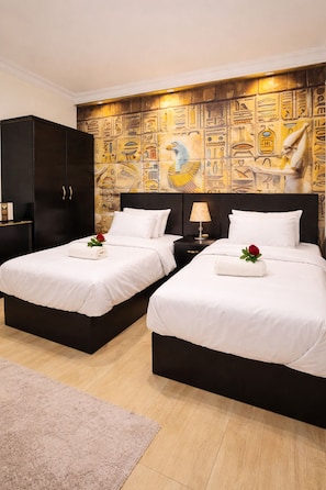 A hotel room with two beds, a dark wardrobe, a wall with Egyptian-themed artwork, and a small rug. - Phoenix Pyramids View Inn (Giza)