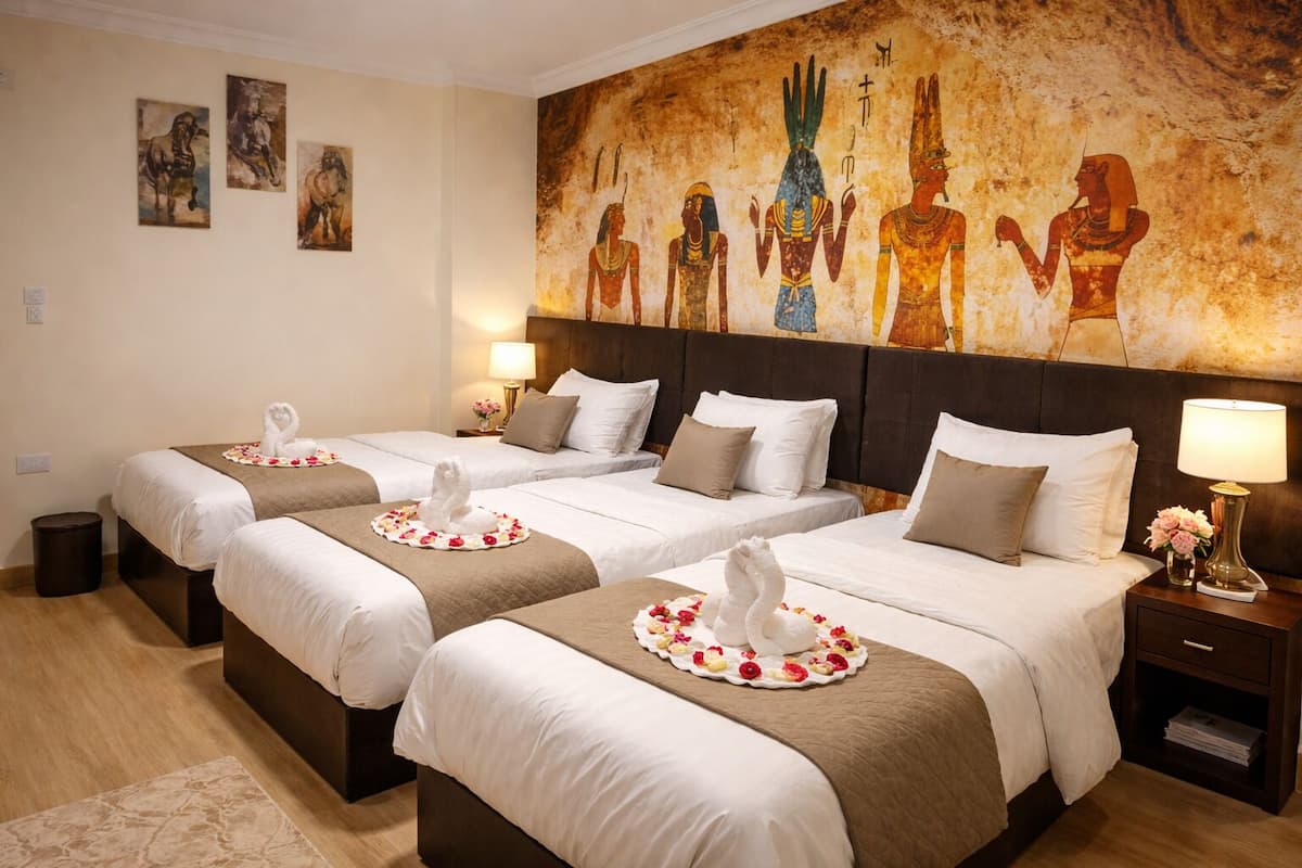 Habitación de hotel con tres camas, un mural grande en la pared y una mesita de noche con una lámpara.
