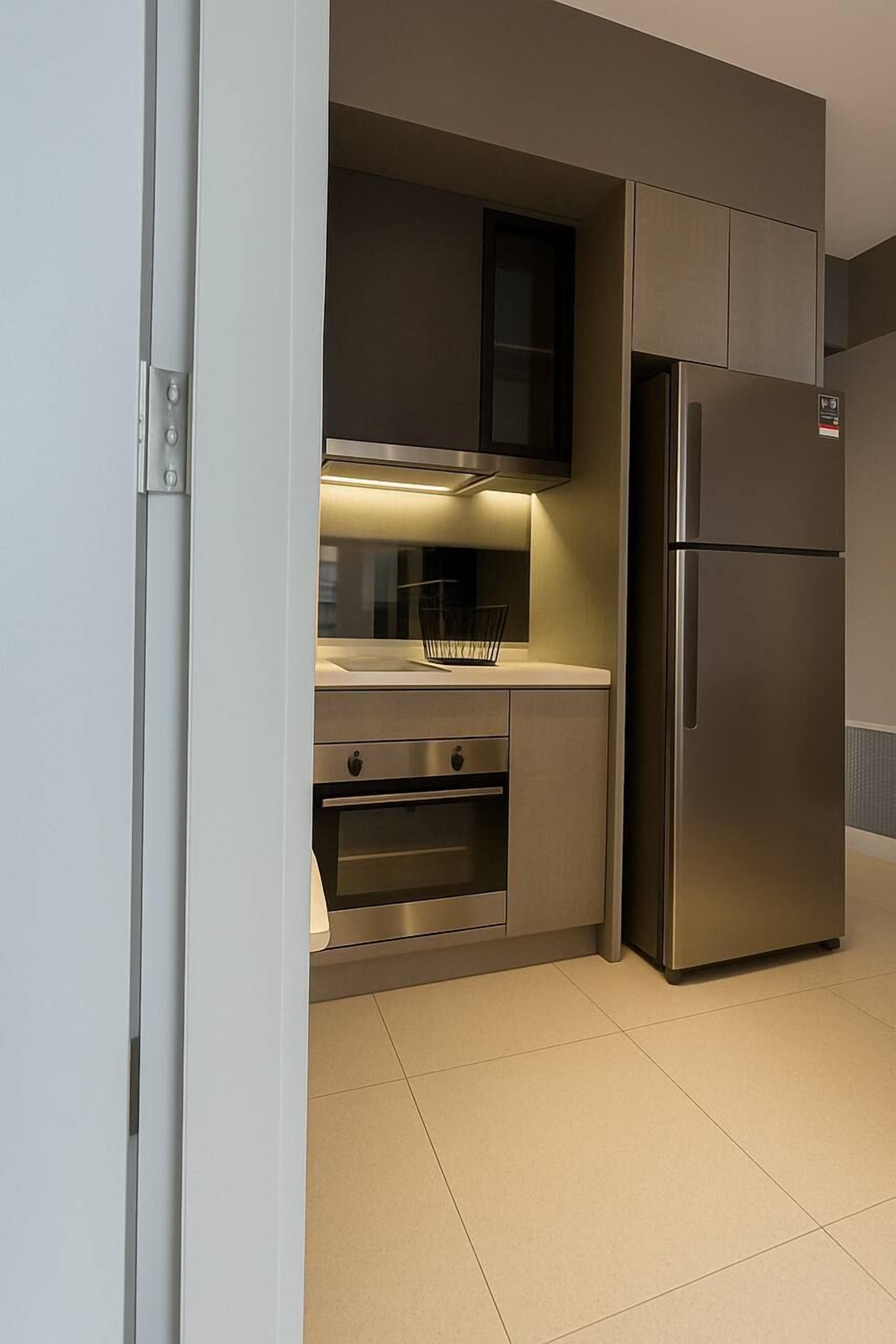 A compact kitchen with a built-in oven, a stainless steel refrigerator, and a microwave.