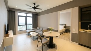 Une chambre d’hôtel moderne équipée d’un canapé, d’une table à manger, d’un ventilateur de plafond et d’une grande fenêtre donnant sur la ville.