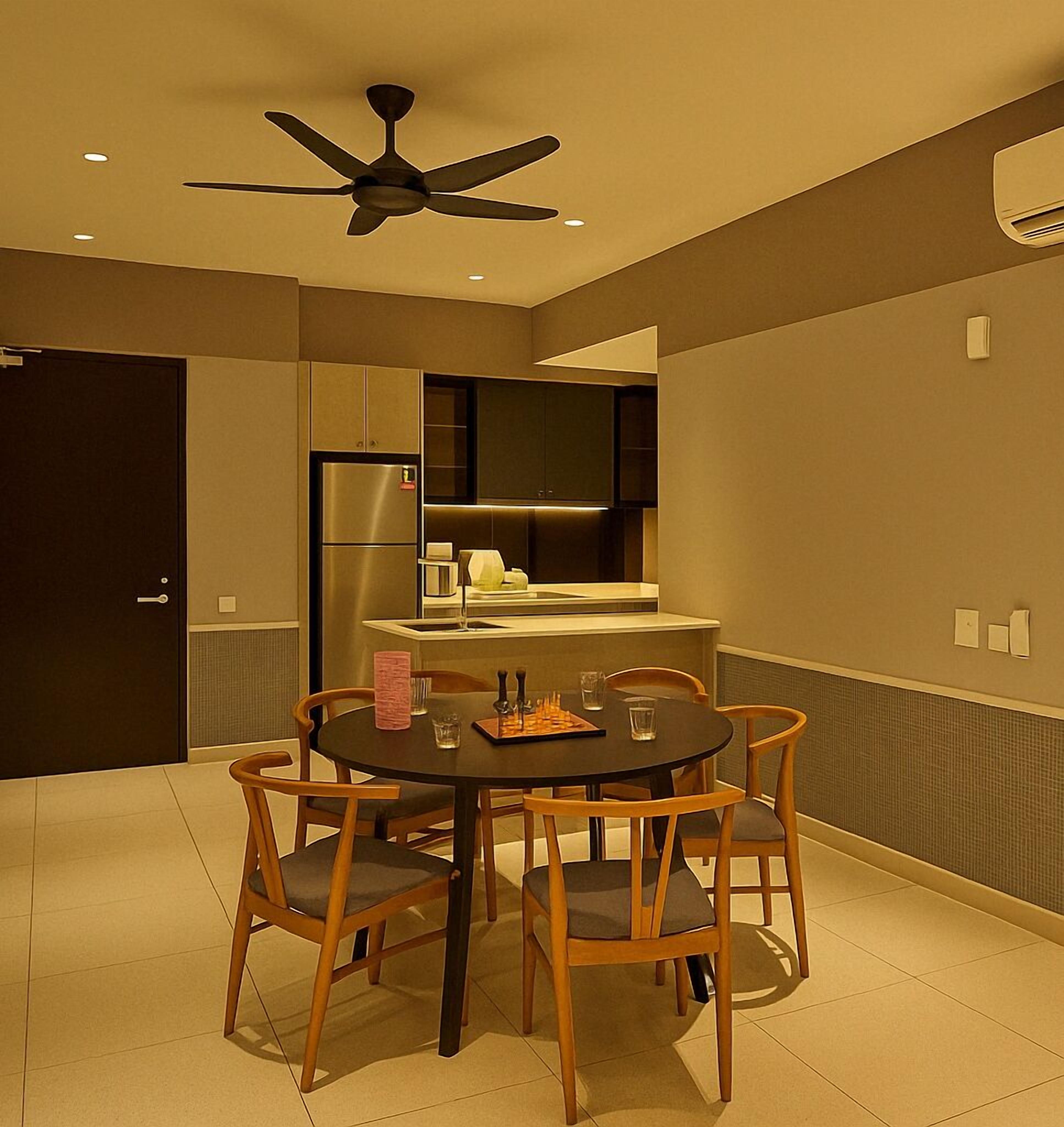 Une cuisine moderne équipée d’un réfrigérateur encastré, d’un four à micro-ondes et d’une cuisinière. On y trouve une table à manger avec quatre chaises, et un ventilateur de plafond au-dessus.