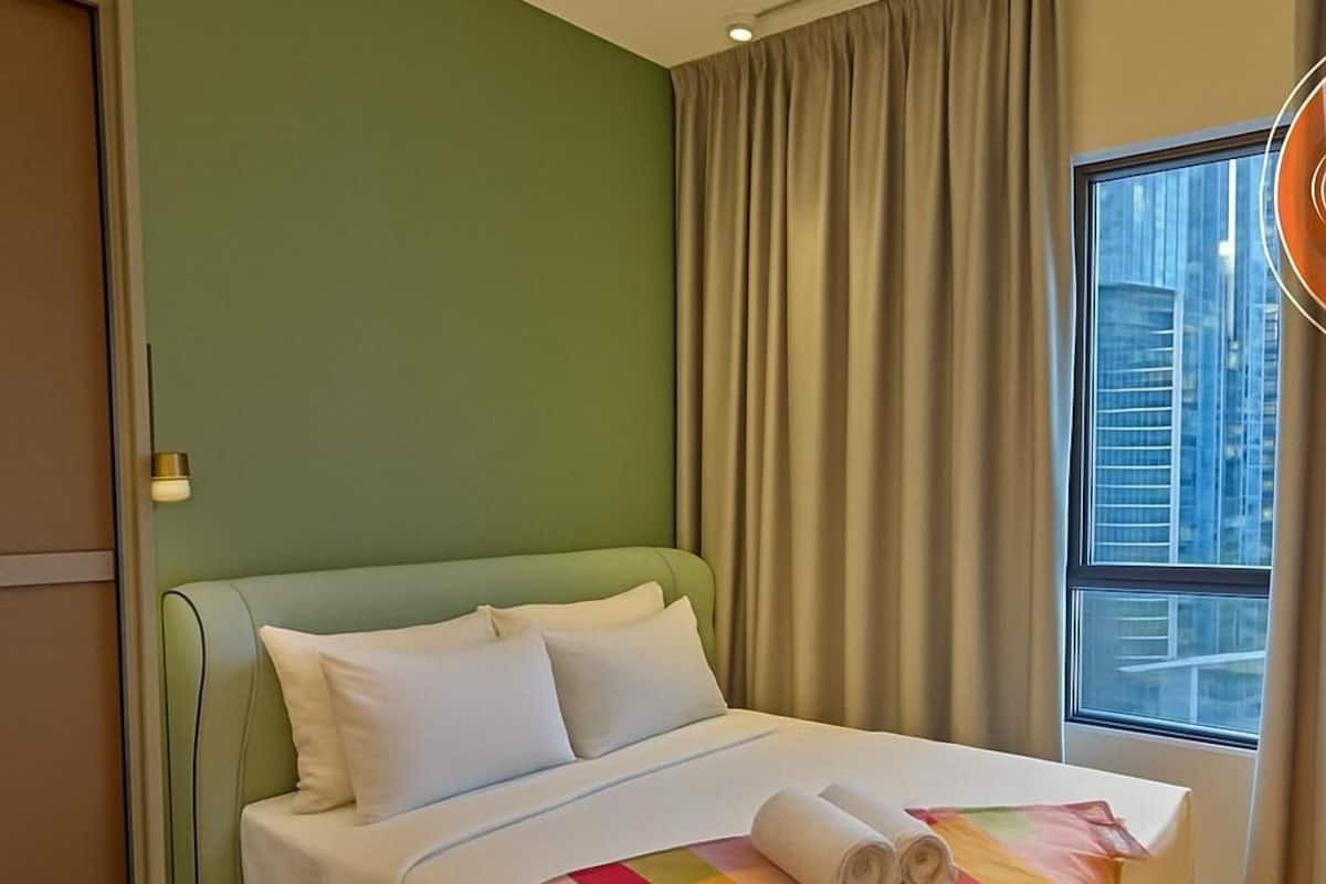 Een hotelkamer met een groene muur, een groot raam met gordijnen, een bed met witte lakens en een regenboogkleed.