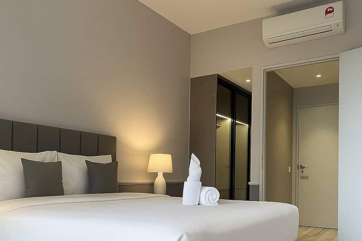 Een hotelkamer met een groot bed, een bedlamp, een airconditioningsapparaat en een deur die naar een andere kamer leidt.