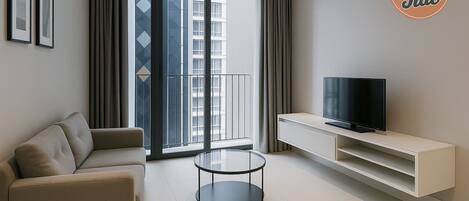 Un soggiorno moderno con un divano, un tavolino in vetro, una TV a schermo piatto su un mobile bianco e una grande finestra con tende.