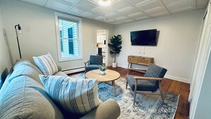 Un salon avec un canapé, des fauteuils, une table basse, un téléviseur et une fenêtre.