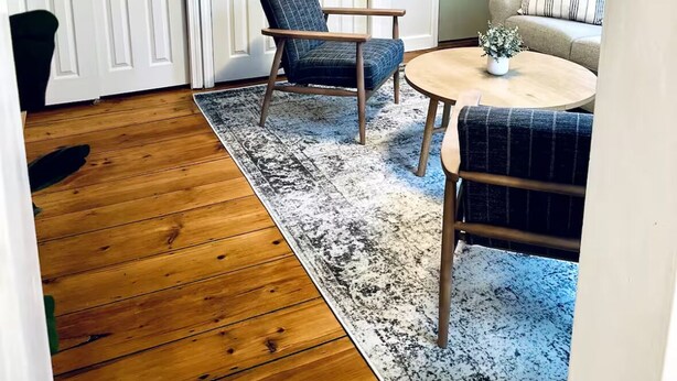 Une pièce avec un plancher en bois, une table ronde, deux chaises, un canapé et un tapis à motifs.