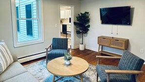Un salon comprenant un canapé, deux fauteuils, une table basse, un téléviseur et une plante en pot.