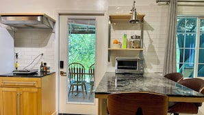 A modern kitchen with a built-in oven, a dining table with chairs, and a view through a glass door to an outdoor area with chairs.