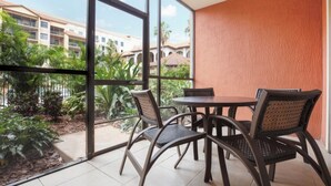 Un balcon avec une table et des chaises, de grandes fenêtres et une vue sur un immeuble et la verdure.