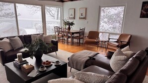 A cozy living room with a dark brown leather sofa, a coffee table with books and a vase, and a dining area with wooden chairs and a table. - Stunning Lake Views To Die For On Lake Arrowhead (Lake Arrowhead)
