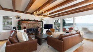 A spacious living room with a stone fireplace, leather sofas, and a large window overlooking a scenic view. - Stunning Lake Views To Die For On Lake Arrowhead (Lake Arrowhead)