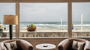 A room with a view of the beach, a potted plant, and two leather chairs.
