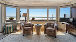 A room with two leather armchairs, a small round table, and a large window overlooking a beach.